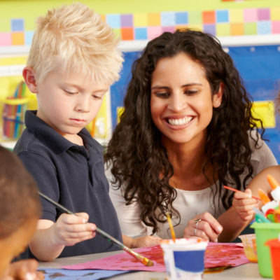 teacher working with young student at an art table