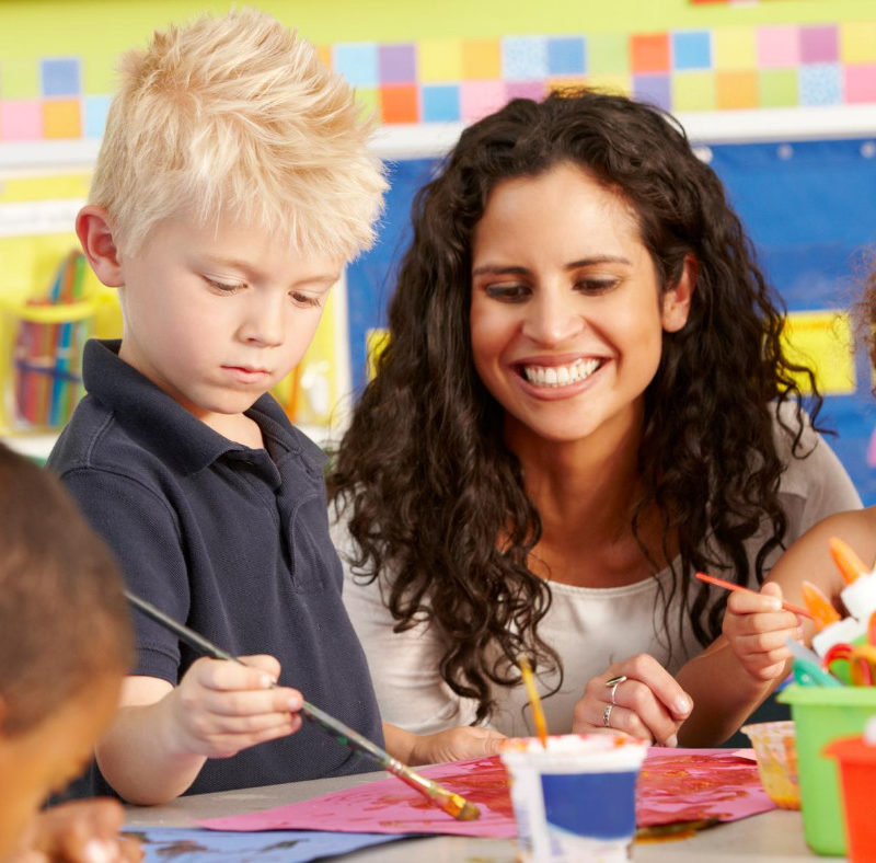 teacher working with young student at an art table