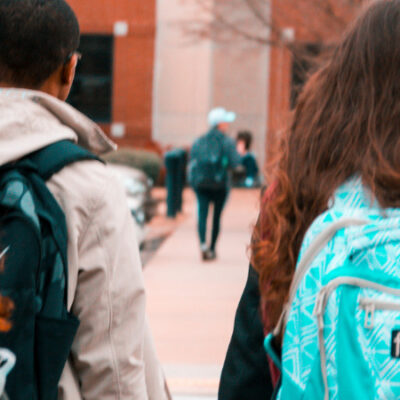 Students walking into school, image from behind so you can only see back of their heads and backpacks