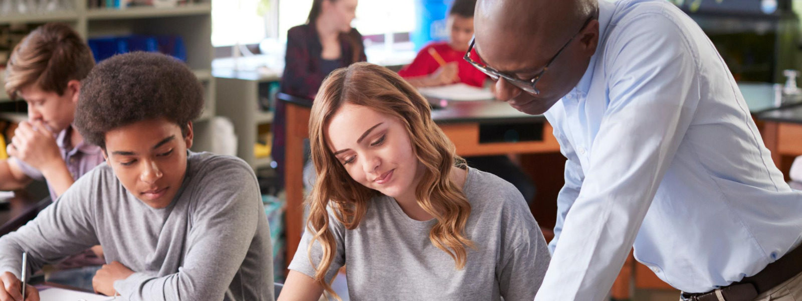 Teacher leaning over students to help them with their assignments