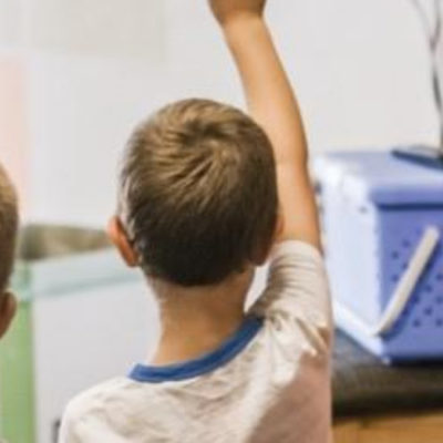 kids in a classroom raising their hands for the teacher